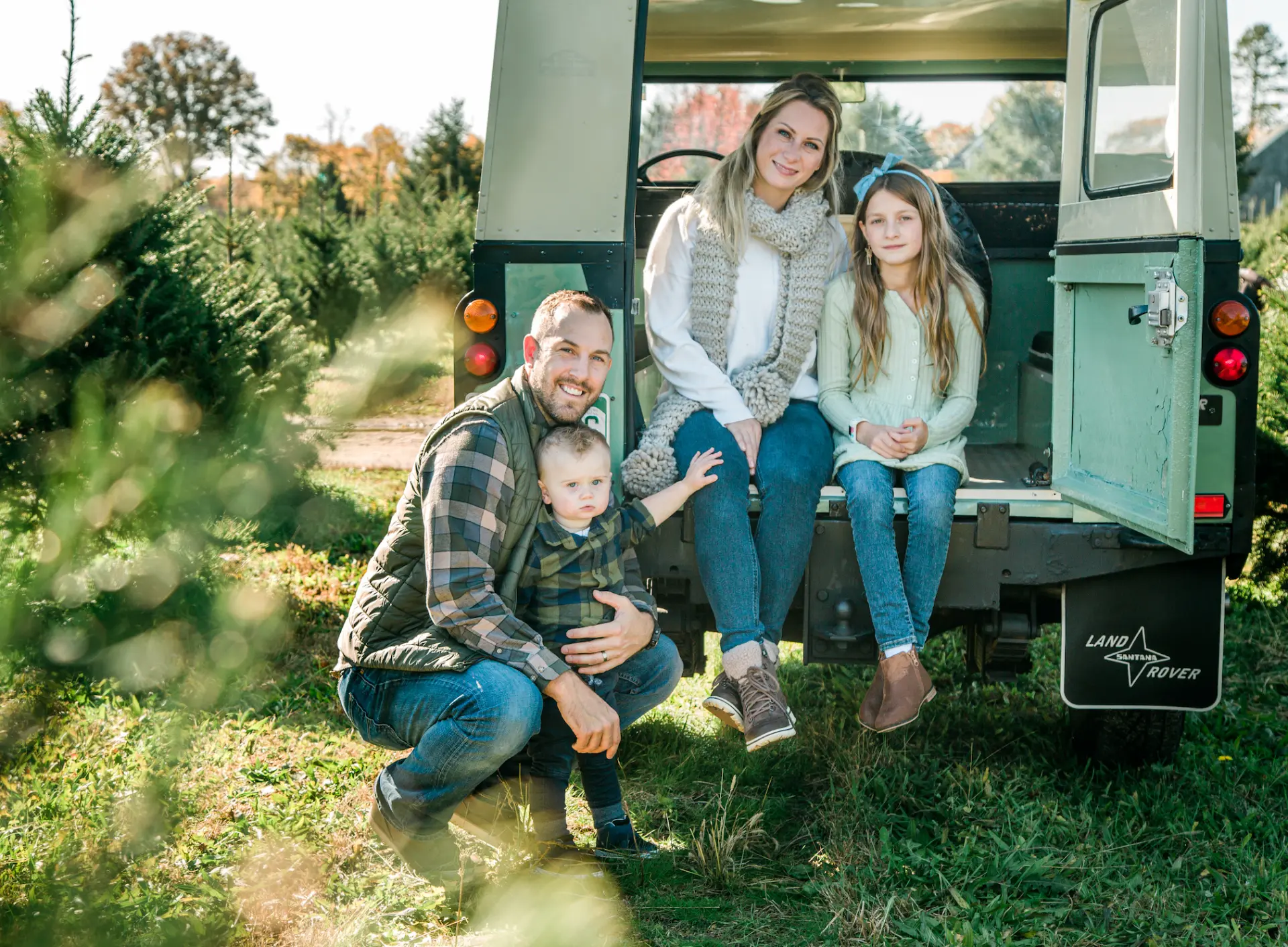 Family of four at the open back of a vintage Land Rover at a Christmas tree farm