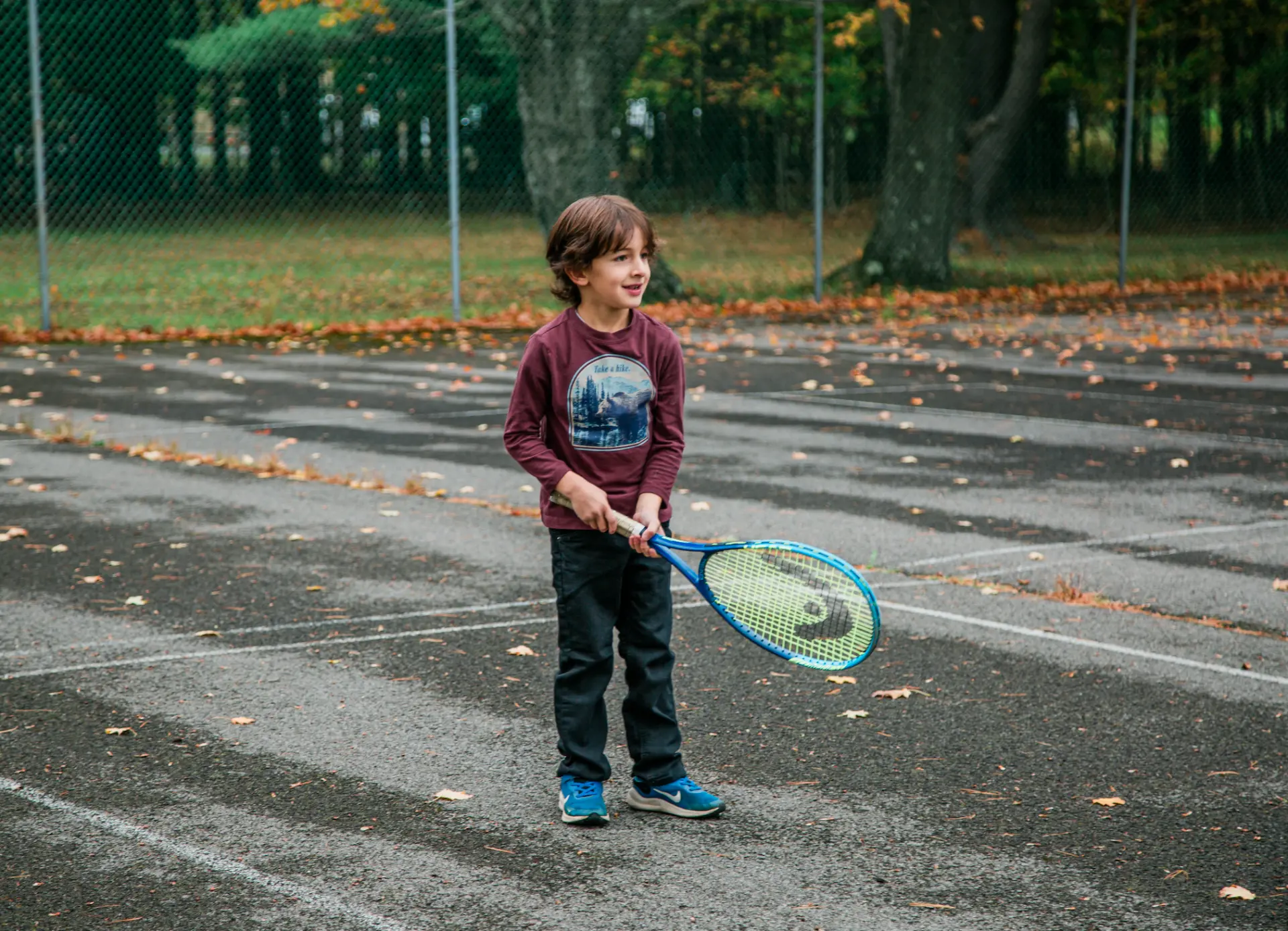Boy with a tennis racket on an autumn tennis court