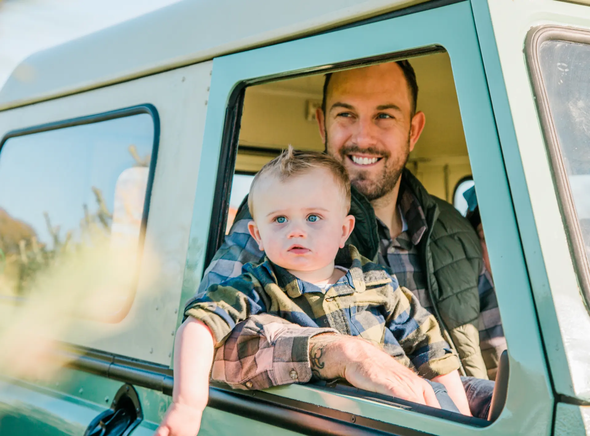 Father and his baby son leaning out the window of a vintage green truck