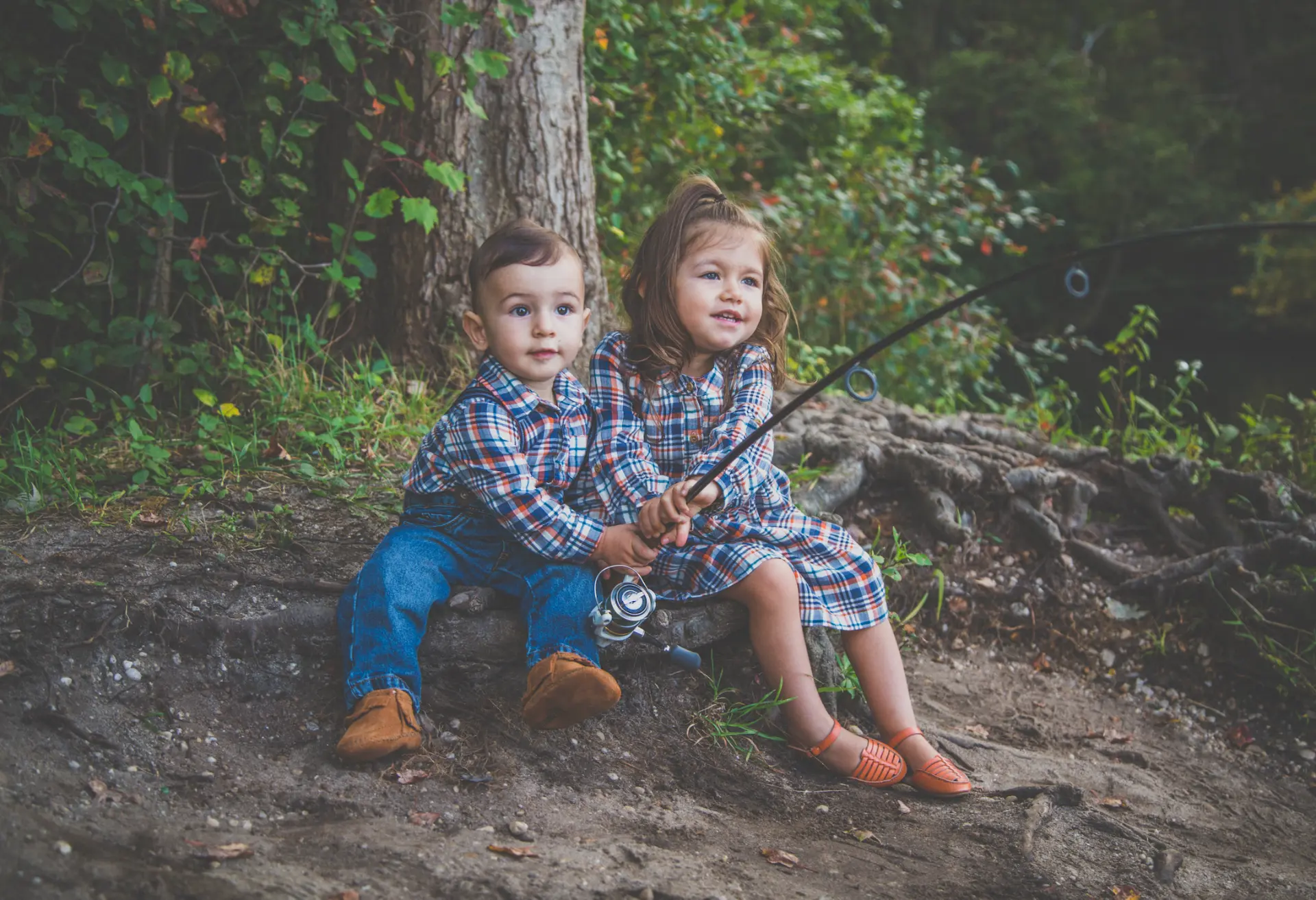 Brother and sister in matching plaid fishing together by a creek