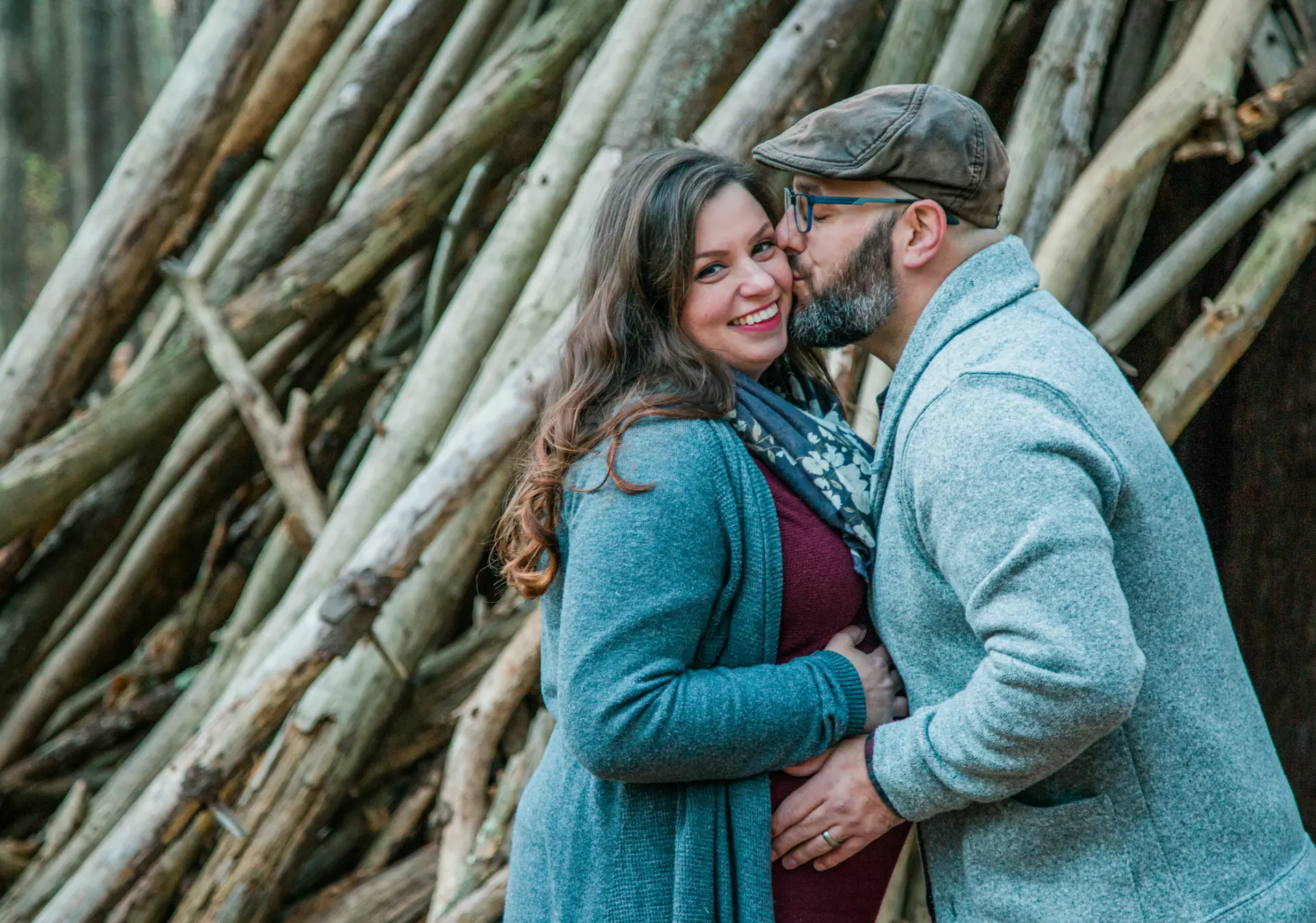Couple embracing while he kisses her cheek against a stack of timber