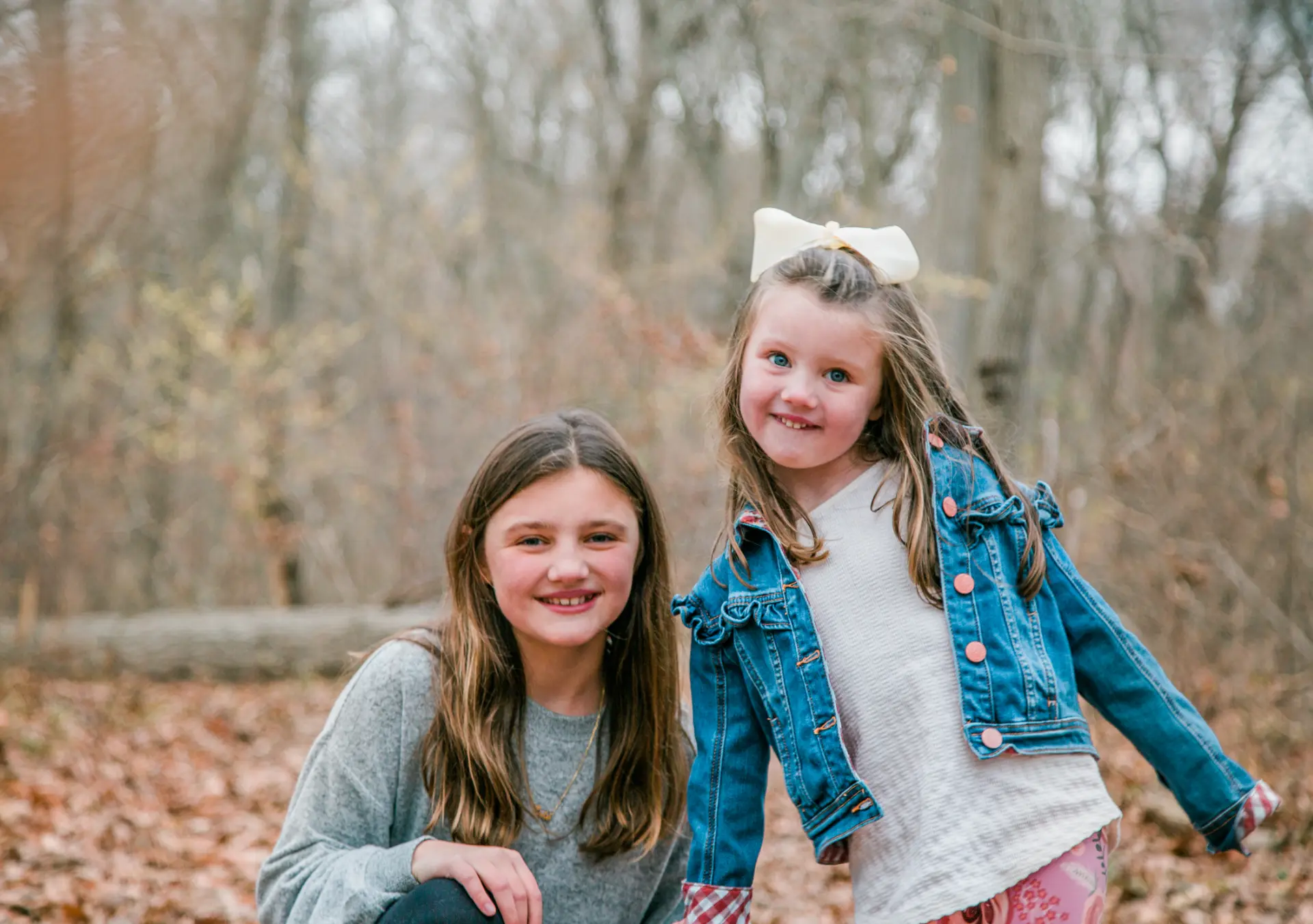 Two sisters smiling together in a leaf-covered winter woods